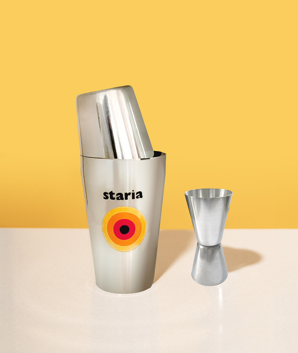 staria cocktail shaker and jigger set on a table against a yellow background